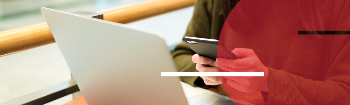 Person holding their smartphone with open laptop